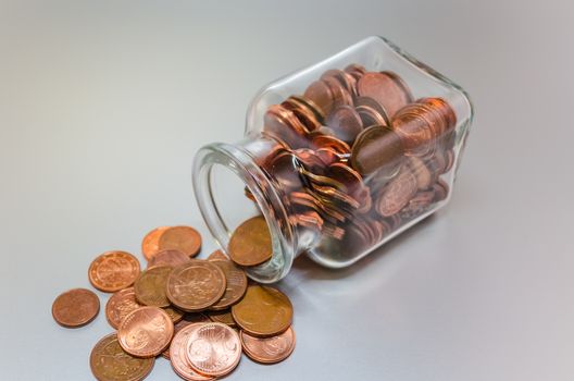 Tilted glass filled with various Euro cent coins.