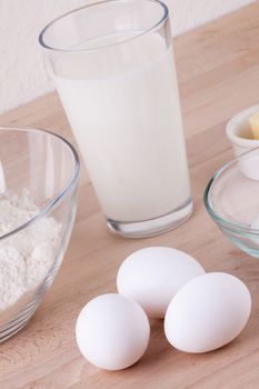 Baking ingredients in the kitchen with a bowl of flour, eggs, sugar, jug of milk and butter ready to bake a cake or make batter