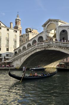 Gondola with tourists crossing the Rialto Bridge, one of the four bridges that spanning the Grand Canal in Venice, Italy. 