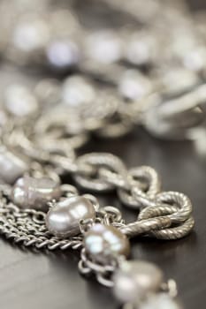 Assorted silver costume jewellery with a jumbled pile of chains with different shaped links, a clear crystal bead and a necklace of round silver beads with focus to the chains