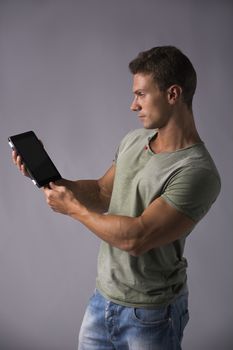 Attractive young man holding ebook reader or tablet PC standing on grey background