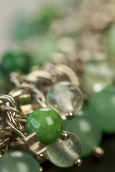 Close up view of pretty translucent green beads on an item of silver jewellery attached in a bunch to a ring by short chains with shallow dof in a fashion concept