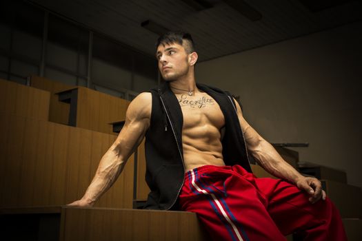 Muscular handsome young man indoor wearing vest on naked torso in abandoned building