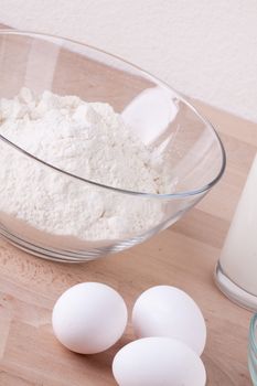 Baking ingredients in the kitchen with a bowl of flour, eggs, sugar, jug of milk and butter ready to bake a cake or make batter