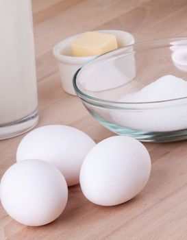 Baking ingredients in the kitchen with a bowl of flour, eggs, sugar, jug of milk and butter ready to bake a cake or make batter