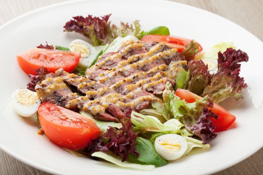 Fresh salad mix with grilled beef, meat cherry tomatoes , boiled quail eggs and  mustard  sauce served on table in white plate