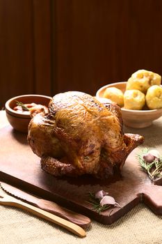 Roast Chicken on wooden board with spices, potatoes and ketchup in the back, photographed with natural light (Selective Focus, Focus on the front of the chicken)  