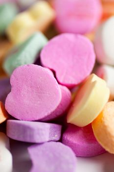 Pastel colored candy hearts in a pile on a white surface.