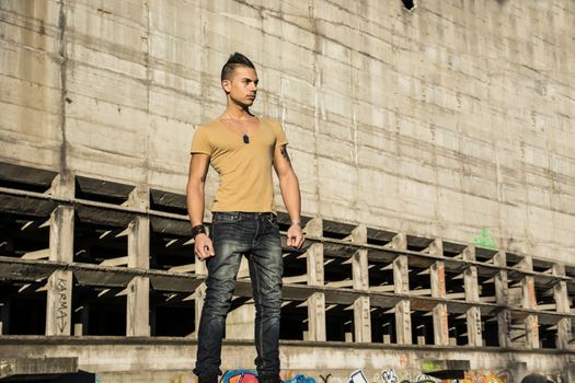 Handsome young man standing in abandoned industrial site outdoor looking away