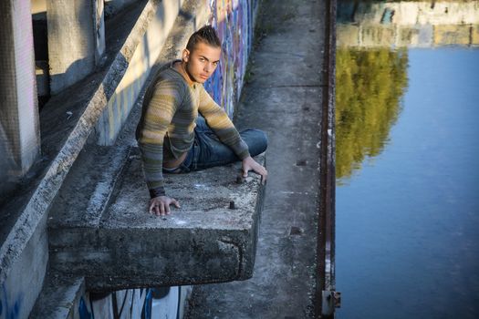 Handsome young man on concrete structure in abandoned industrial site