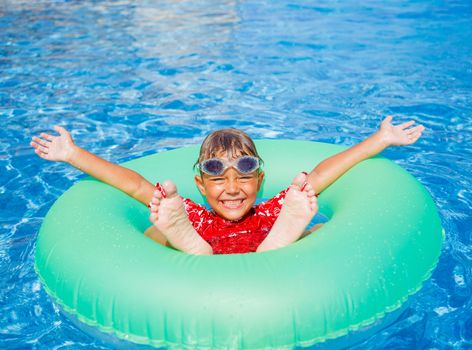 Cute little boy swims in a pool in an green life preserver