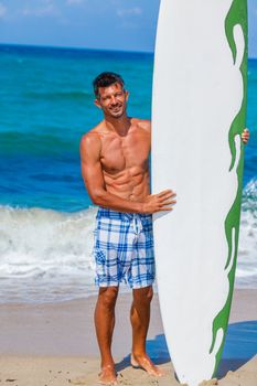 Strong young surf man at the beach with a surfboard.