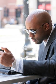 A business man in his early 30s working on his laptop or netbook computer outdoors.