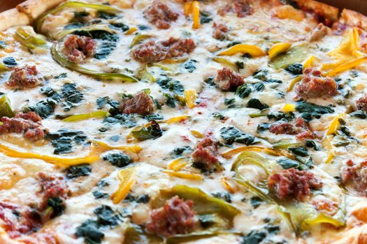 Close up detail of a fresh specialty pizza with spinach peppers and sausage.  Shallow depth of field.