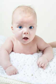 A cute newborn baby boy on a white blanket laying on his belly with mothers arm around him.