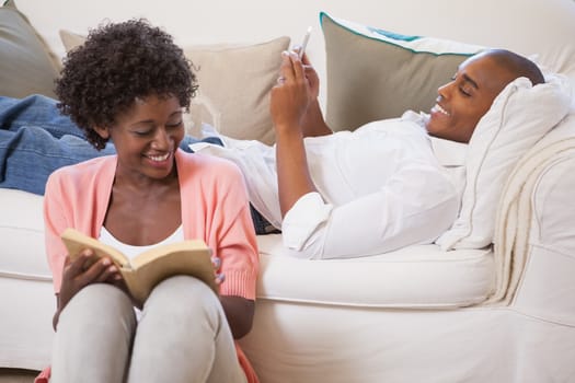 Happy couple relaxing together reading book and using smartphone at home in the living room