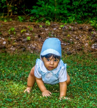 Latino baby dressed up and crawling outside in the grass