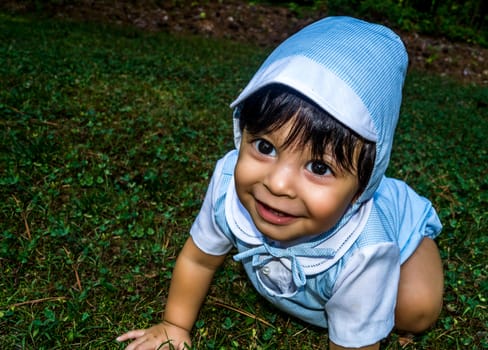 Close up shot of smiling latino baby dressed up and crawling outside in the grass