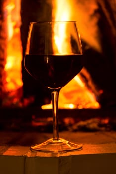 Glass of red vine near burning fireplace