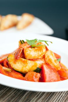 Thai style sweet and sour shrimp dish presented beautifully on a round white plate. Shallow depth of field.