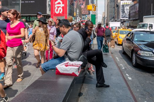 New York - Aug 20: Pedestrians walk by a two guys sitting on a concrete bench on the the busy streets of downtown New York on August 20, 2014 in New York, USA