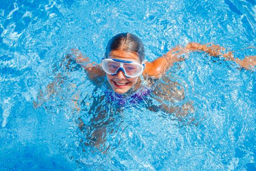 Cute happy young girl in goggles swimming and snorking in the swimming pool