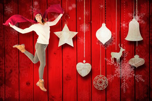 Happy brunette jumping and holding his scarf against christmas decorations over wood