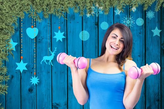 Smiling fit brunette holding dumbbells against christmas decorations over wooden planks