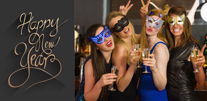 Attractive women wearing masks holding champagne against classy new year greeting