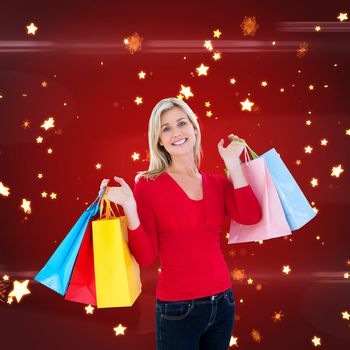 Happy blonde holding shopping bags against bright star pattern on red