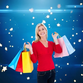 Happy blonde holding shopping bags against bright star pattern on blue