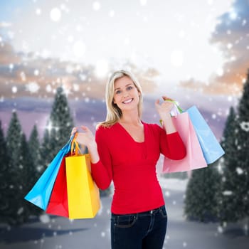 Happy blonde holding shopping bags against snowy landscape with fir trees