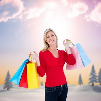 Happy blonde holding shopping bags against snowy landscape with fir trees