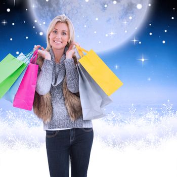 Blonde in winter clothes holding shopping bags against white clouds under blue sky