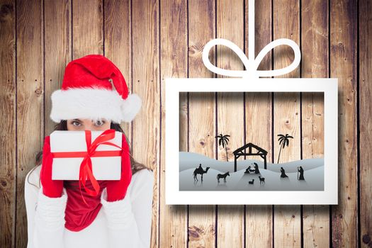 Brunette in red gloves and santa hat showing gift against christmas decorations over wood
