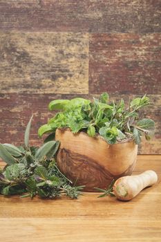 Different culinary herbs in a mortar over rustic table
