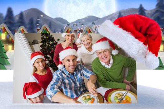 Father in santa hat carving chicken at christmas dinner against quaint town with bright moon