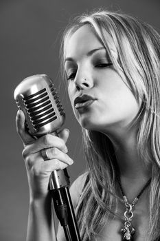 Photo of a beautiful young blond singing into a vintage microphone done in black and white.