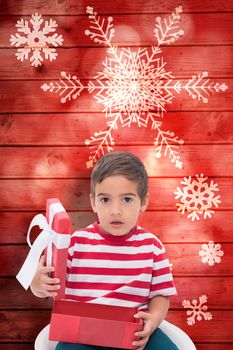 Cute little boy opening gift against snowflake pattern on red planks