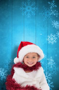 Cute little girl wearing santa hat and tinsel against snowflake pattern on blue planks