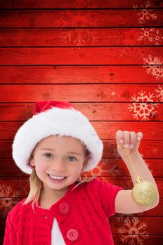 Cute little girl wearing santa hat holding bauble against snowflake pattern on red planks