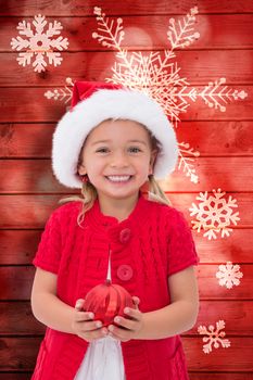 Cute little girl wearing santa hat holding bauble against snowflake pattern on red planks