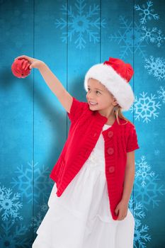 Cute little girl wearing santa hat holding bauble against snowflake pattern on blue planks