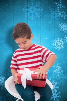 Cute little boy opening gift against snowflake pattern on blue planks