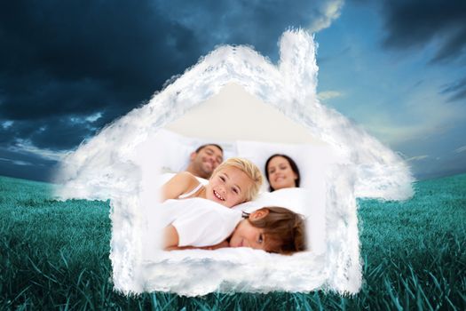 Family realxing in parents bed against blue sky over green field