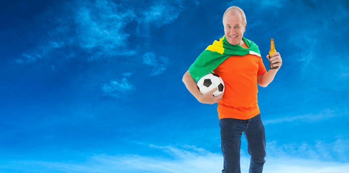 Mature man in orange tshirt holding football and beer against blue sky