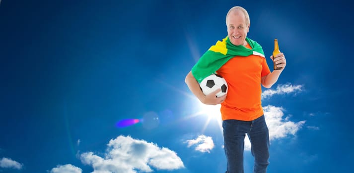 Mature man in orange tshirt holding football and beer against cloudy sky with sunshine