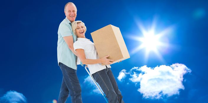 Fun older couple holding moving boxes against bright blue sky with clouds