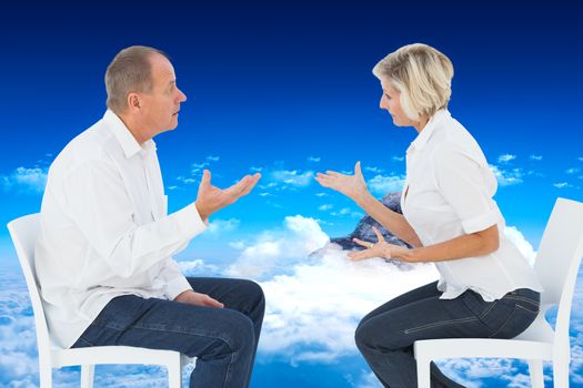 Older couple sitting in chairs arguing against mountain peak through clouds