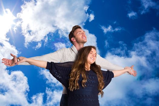 Romantic young couple with arms out against bright blue sky with clouds